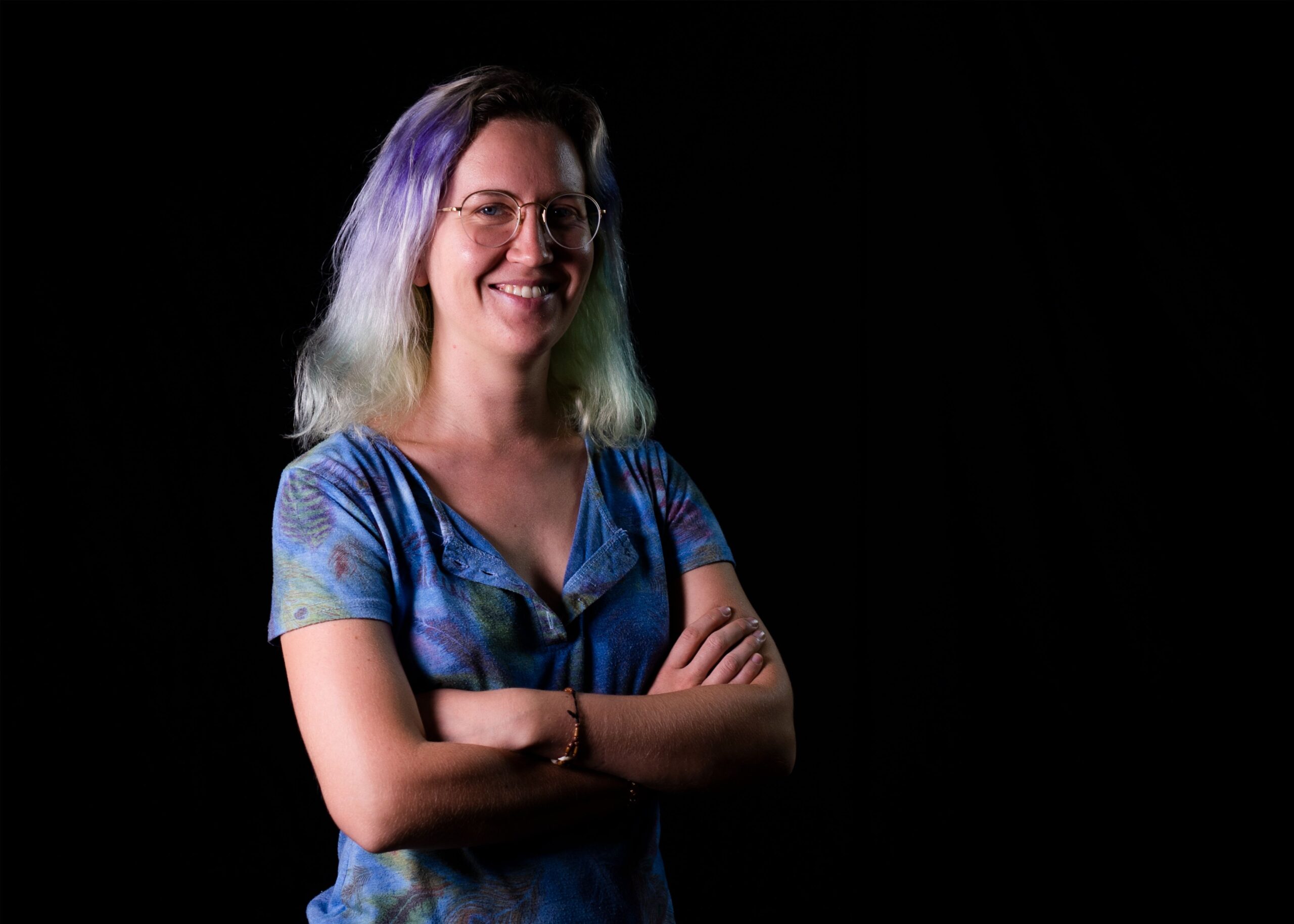 Smiling woman with colorful hair and glasses on black background.